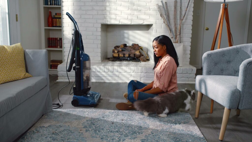 girl has a staredown with her old busted vacuum cleaner in front of a white fireplace